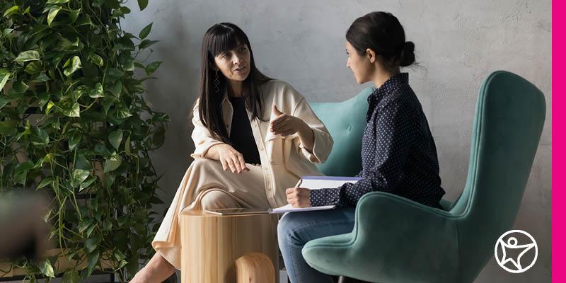 Two professional women sitting in chairs and engaged in a conversation